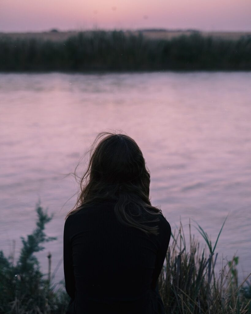 Woman sitting by a calm lake at dusk